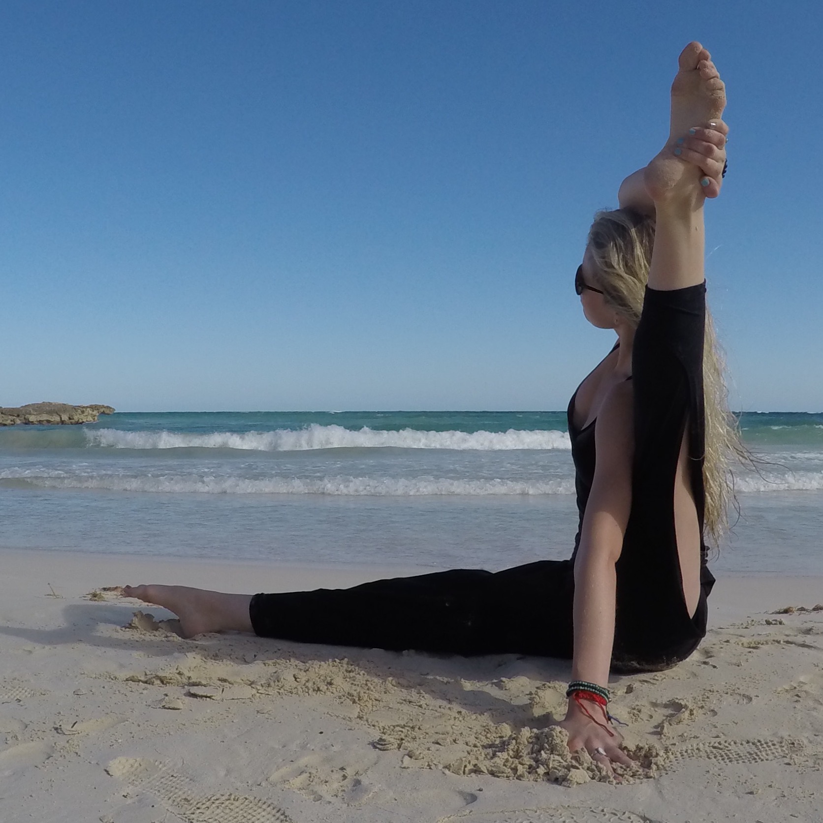 Ellery Long with legs lifted on a sunlit beach